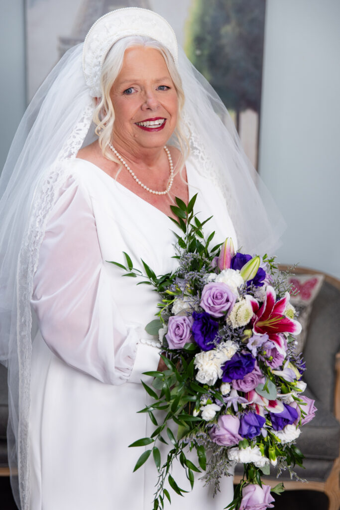 bride holding purple, white and red bouquet wearing a white dress and handmade 1974 veil