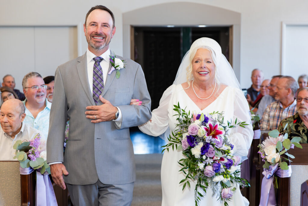 elderly bride walking down the aisle with son smiling during 50th vow renewal at The Abbey