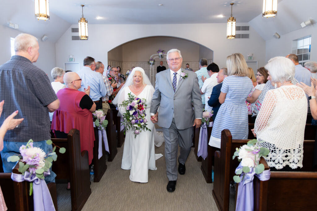 elderly bride and groom walking down the aisle smiling after The Abbey 50th vow renewal