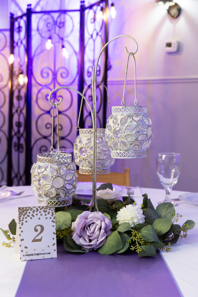 elegant 3 tier-candle holder centerpiece for wedding at The Abbey venue surrounded by greenery, purple flowers and purple uplighting