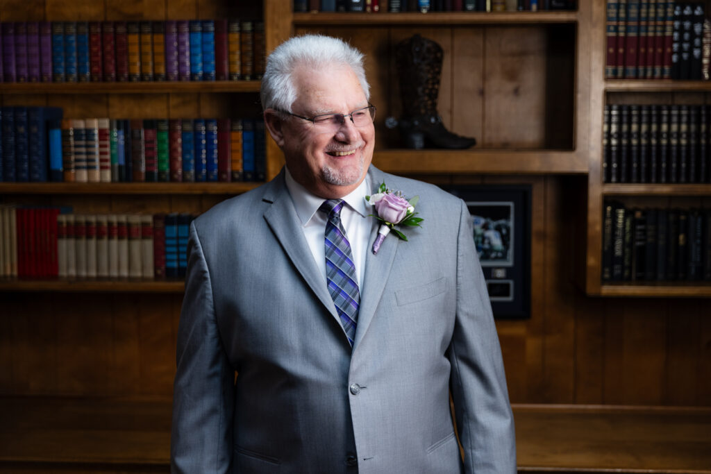 groom smiling in grey suit in The Abbey's groom suite library