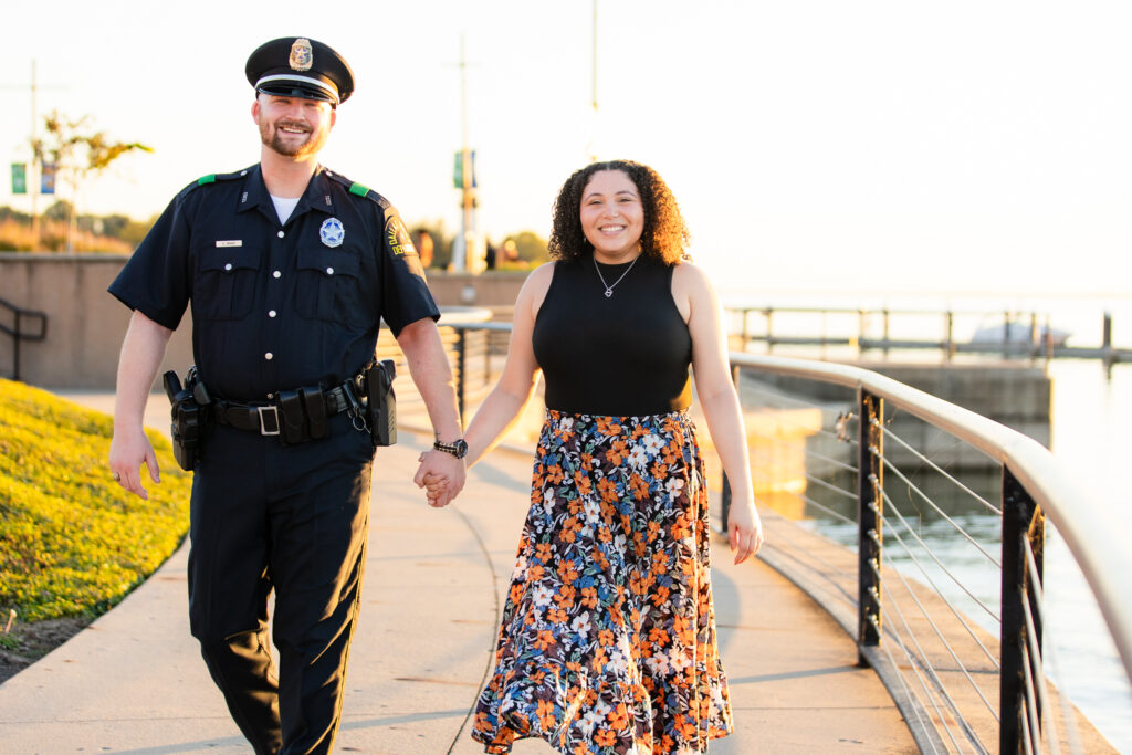 happily engaged couple holding hands and walking along lake shore at sunset