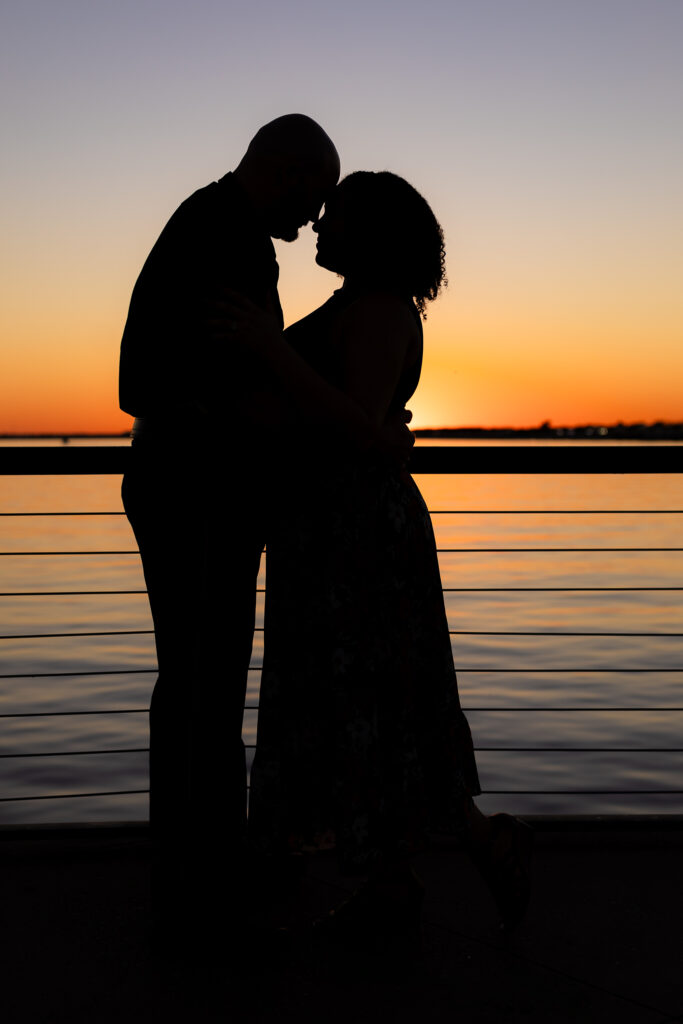 engaged couple silhouetted hugging at sunset by lake in Rockwall