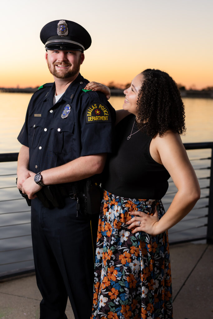 engaged woman smiling up at fiancé wearing police uniform in Rockwall during engagement session at sunset