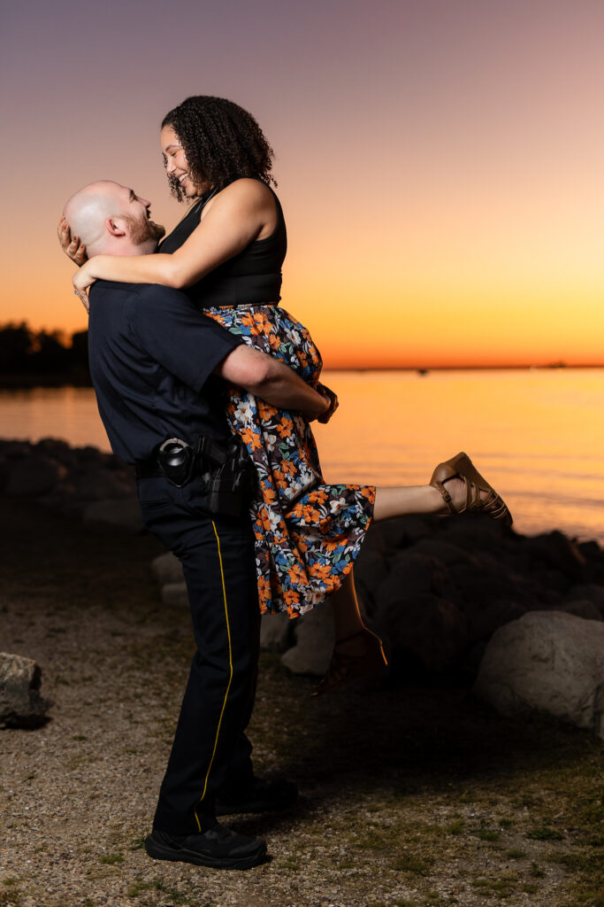 man in police uniform lifting fiancée with leg in the air at sunset in Rockwall during engagement session