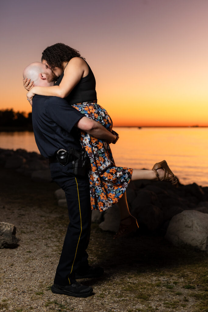 man in police uniform lifting fiancée while kissing at sunset in Rockwall during engagement shoot