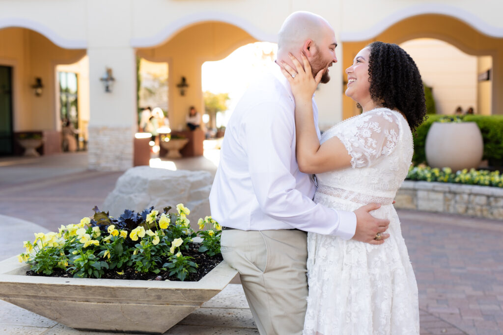 engaged woman grabbing fiancé's face smiling at each other wearing all white during Rockwall engagement session