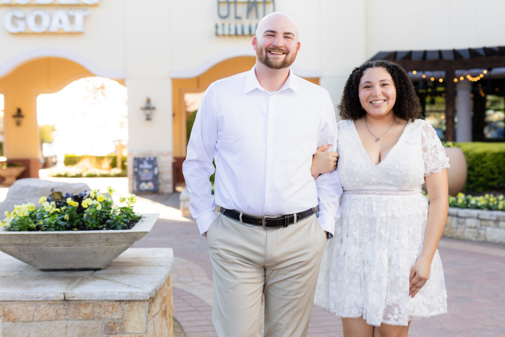 engaged couple linking arms walking and smiling toward camera