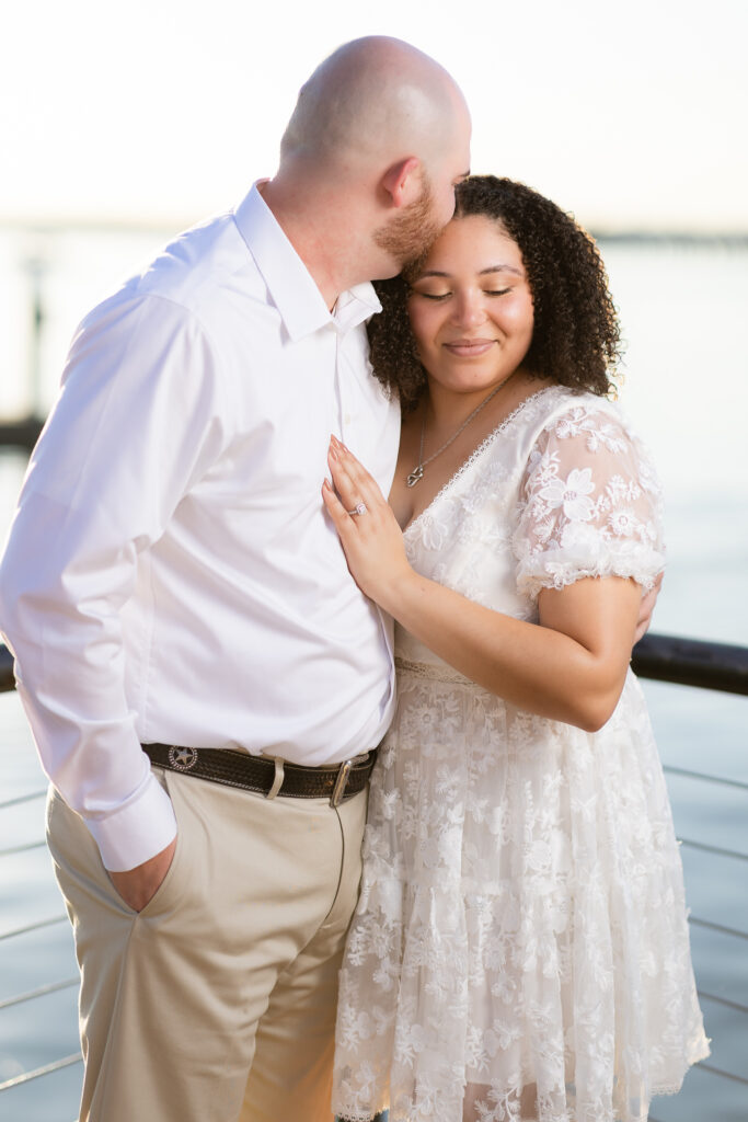 Man kissing fiancée on forehead at Rockwall lake during engagement session in Texas