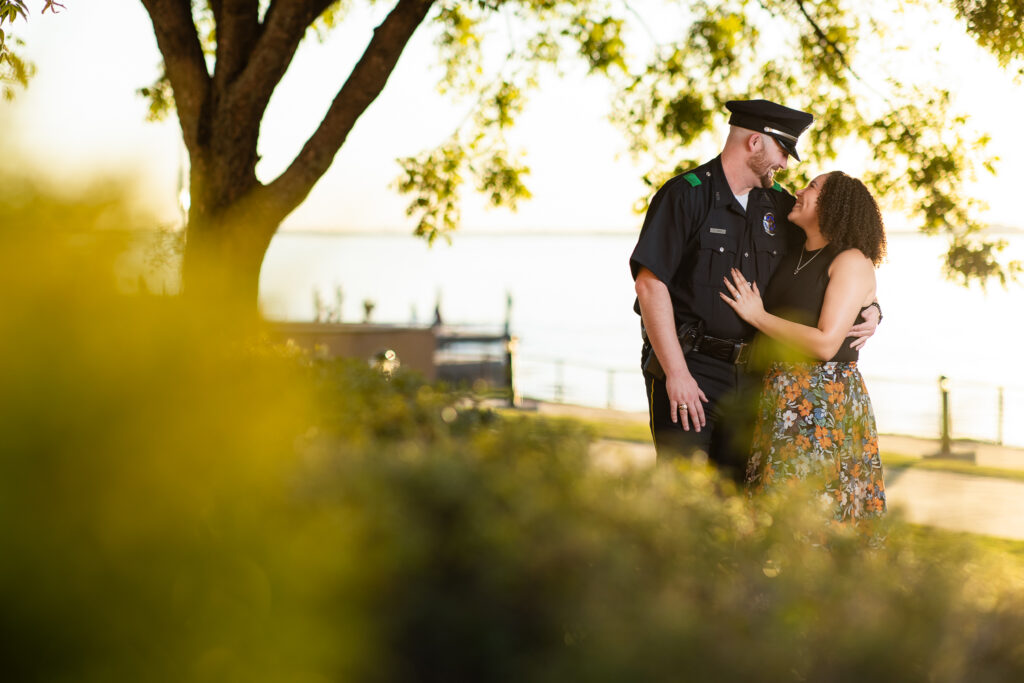 engaged couple cuddling under big tree while smiling at each other during Rockwall engagement session