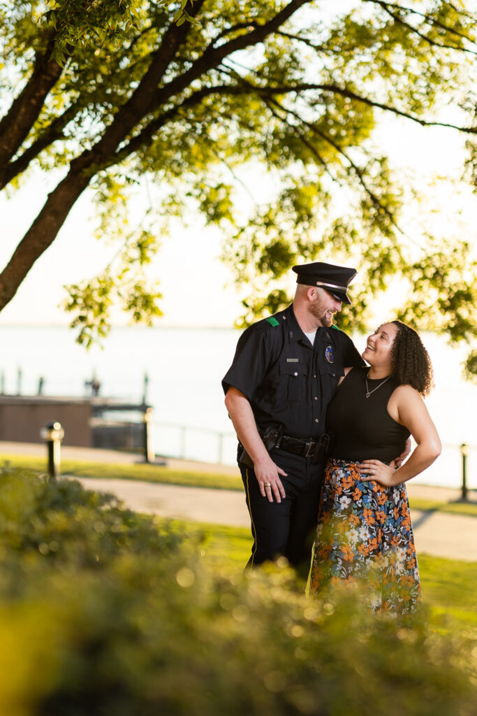 engaged couple smiling at each other under big tree in Rockwall at golden hour