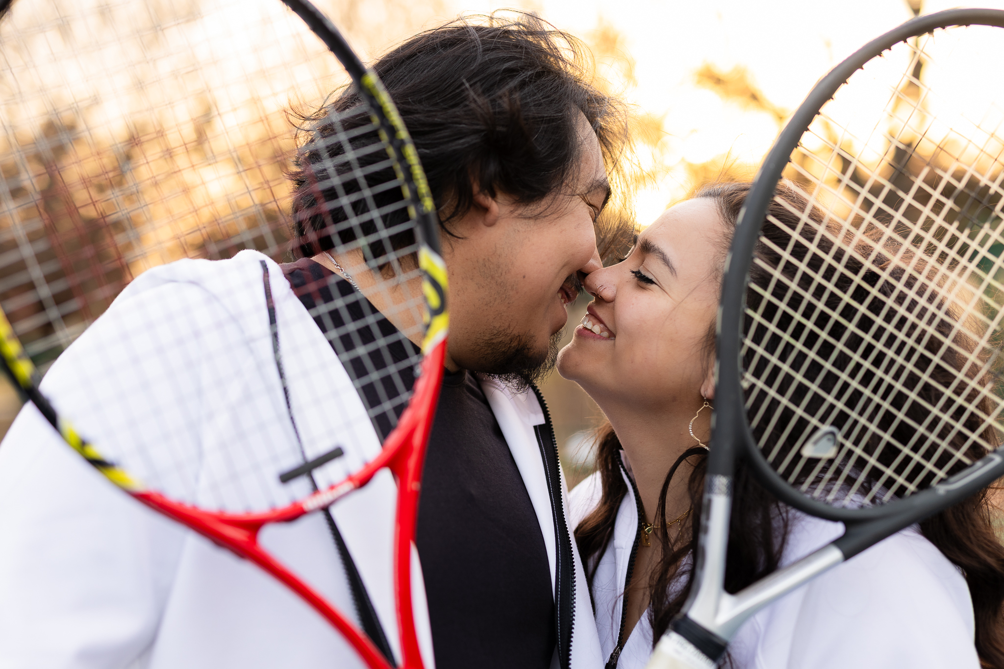 Couple almost kissing and smiling with tennis rackets in front of them during Monticello Park Tennis Courts engagement session