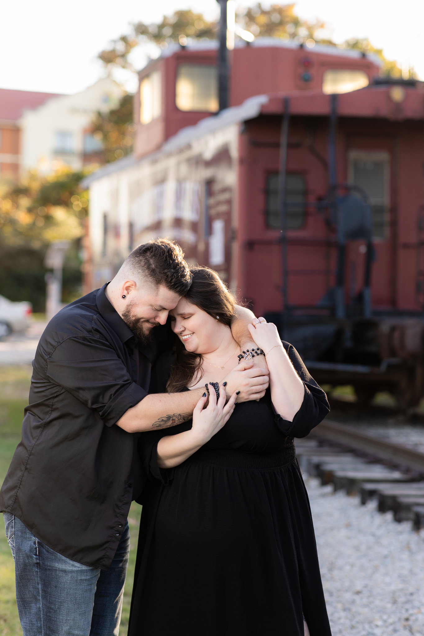 Couple cuddling and hugging in front of train at the Stockyards in Fort Worth for engagement photos